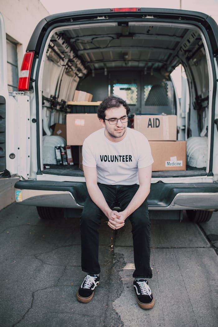 A volunteer sits in front of a supply-filled van, ready for aid distribution.